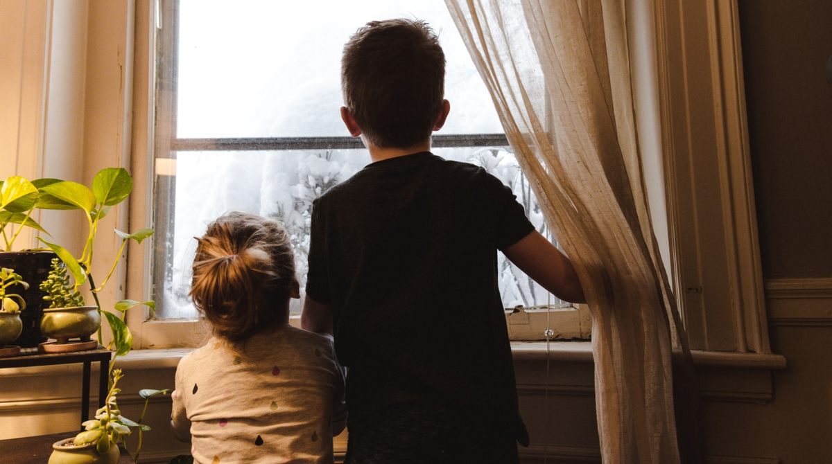 Two children looking out of a frosted window into a rainy backyard.
