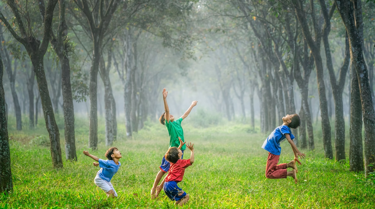 Four children playing ball in a clearing surrounded by trees.