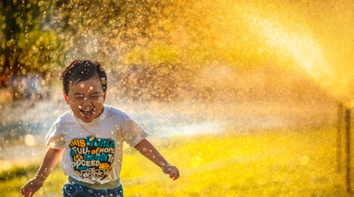 A toddler runs through a sprinkle of water and sunlight.